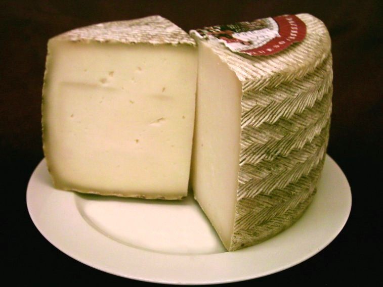 Un morceau de fromage Manchego sur une assiette, montrant la croûte tissée et la texture crémeuse à l'intérieur.